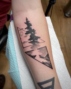 a person with a tattoo on their arm that has mountains and trees in the background