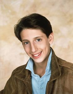 a young man wearing a brown jacket and smiling