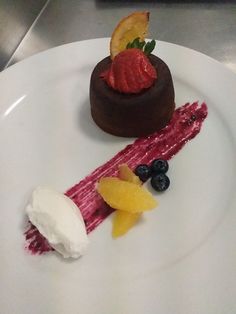 a white plate topped with a piece of cake and fruit on top of ice cream