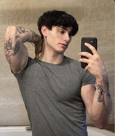 a man taking a selfie with his cell phone in front of him and tattoos on his arm