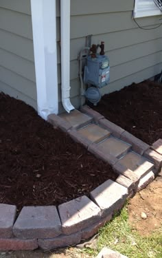 a fire hydrant in the corner of a house next to a flower bed with mulch