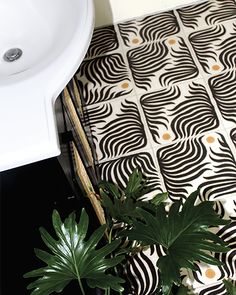 a bathroom with black and white patterned flooring next to a plant on the ground