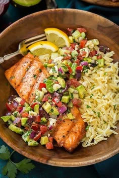 salmon, rice and vegetables in a wooden bowl with lemon wedges on the side