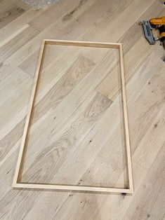 a wooden frame sitting on top of a hard wood floor next to a hammer and screwdriver