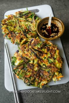 some food is sitting on a cutting board with chopsticks and sauce in the background