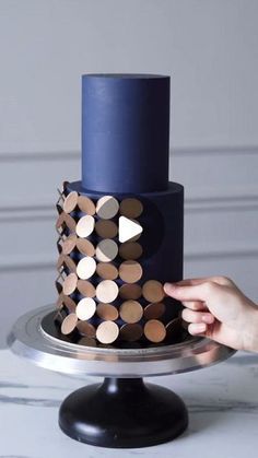 a woman is decorating a blue cake with wooden circles on it and the top tier is made out of wood slices