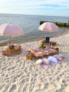 an outdoor picnic on the beach with pink umbrellas and food set up for two