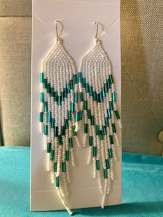 white and green seed beaded earrings on display in front of a blue cushioned chair