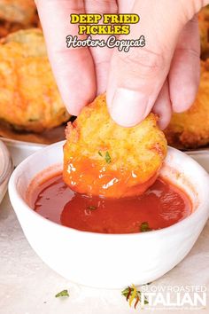 a person dipping something into a bowl of tomato sauce with a hand reaching for it