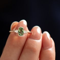 a woman's hand holding an engagement ring with a green stone and diamond accents