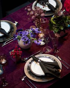 the table is set with black and white plates, silverware, and purple flowers