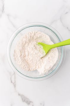 a glass bowl filled with white powder and a green plastic spoon on a marble counter top