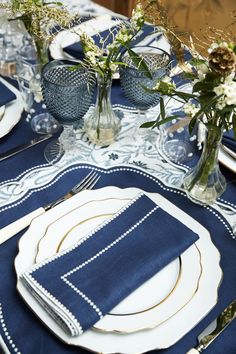 the table is set with blue linens and white placemats, silverware, and flowers