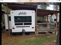 an rv parked under a covered porch in front of a tree and fenced off area