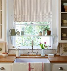 a kitchen sink under a window next to a shelf with dishes and cups on it