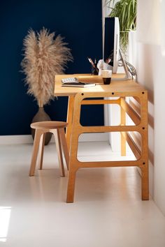 a wooden desk with a plant on it next to a white chair and blue wall