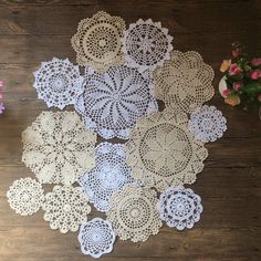 an assortment of crocheted doily on a wooden table with flowers in the background