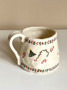 a white mug with christmas decorations on it sitting on top of a table next to a wall