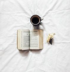 an open book, coffee cup and flower on a white sheet