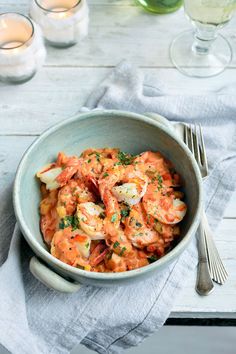 a bowl filled with shrimp and garnished with parsley next to wine glasses