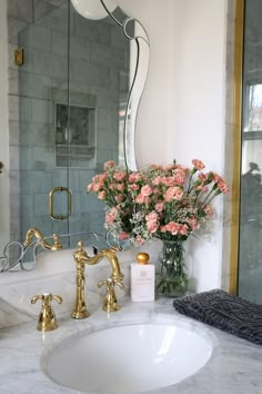 a white sink sitting under a bathroom mirror next to a vase with flowers in it