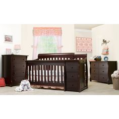 a baby crib in a room with two dressers and a teddy bear on the floor