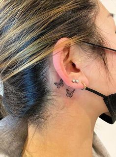 a woman with a small butterfly tattoo on her left side behind the ear is wearing a black ribbon