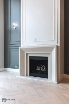 an empty room with a fireplace in the center and white cabinets on either side, along with parquet flooring