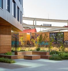 an urban park with benches and plants in the foreground, under a bridge overpass