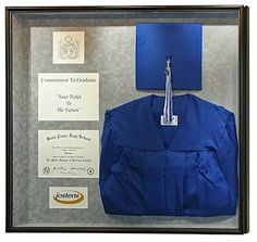 a blue graduation cap and gown hanging in a glass case with certificate on the wall