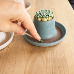 a person is holding a match stick in a small cup on a wooden table next to a plate