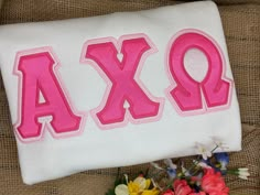 an embroidered pillow with the word ajax on it and some flowers in front of it