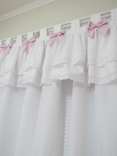 pink bows are hanging on the curtain rod in front of white curtains with ruffles