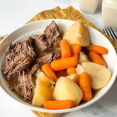 a bowl filled with meat, potatoes and carrots next to a glass of milk