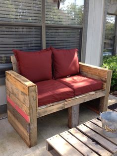 a wooden bench sitting on top of a patio next to a red cushioned couch