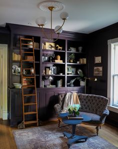 a living room filled with furniture and bookshelves next to a window in front of a ladder