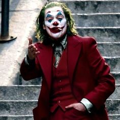 a man dressed in a red suit and clown makeup is standing on the steps with his finger up