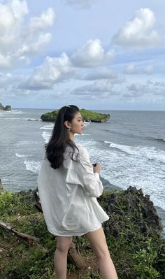 a woman standing on top of a lush green hillside next to the ocean