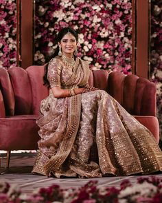 a woman sitting on top of a couch wearing a gold and pink dress with flowers in the background