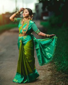 a woman in a green and gold sari dancing on the side of a road