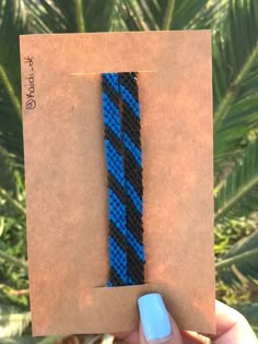 a hand holding up a blue and black bracelet with an arrow on the side, in front of a palm tree