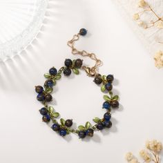 a bracelet with blue beads and green leaves on it next to some dried white flowers