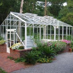 a small greenhouse in the middle of a brick garden area with lots of plants and flowers