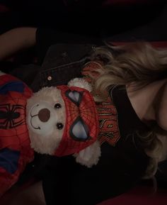 a woman laying on top of a bed next to a spiderman teddy bear wearing a shirt