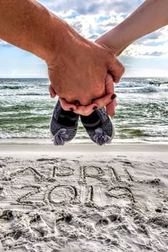 two people holding hands while standing in the sand at the beach that says love you