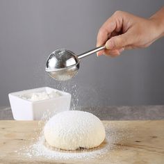 a person sprinkling sugar onto a doughnut on top of a wooden table