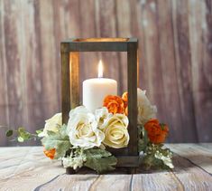 a white candle with orange and yellow flowers in a wooden lantern holder on a table