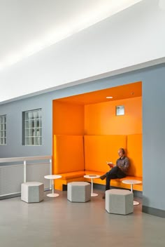 a man sitting on an orange couch in a room with white tables and stools