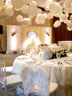 a banquet table with white chairs and paper lanterns hanging from the ceiling