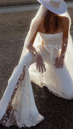 a woman sitting on the ground wearing a white dress and hat